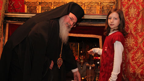 Der griechisch-orthodoxe Bischof Theofilaktos von Bethlehem  übergibt das ORF-Friedenslicht in der Geburtstgrotte an das Friedenslichtkind Sarah Schinwald aus Munderfing