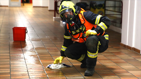 Feuerwehrmann mit Gasmaske wischt stinkende Flüssigkeit vom Boden