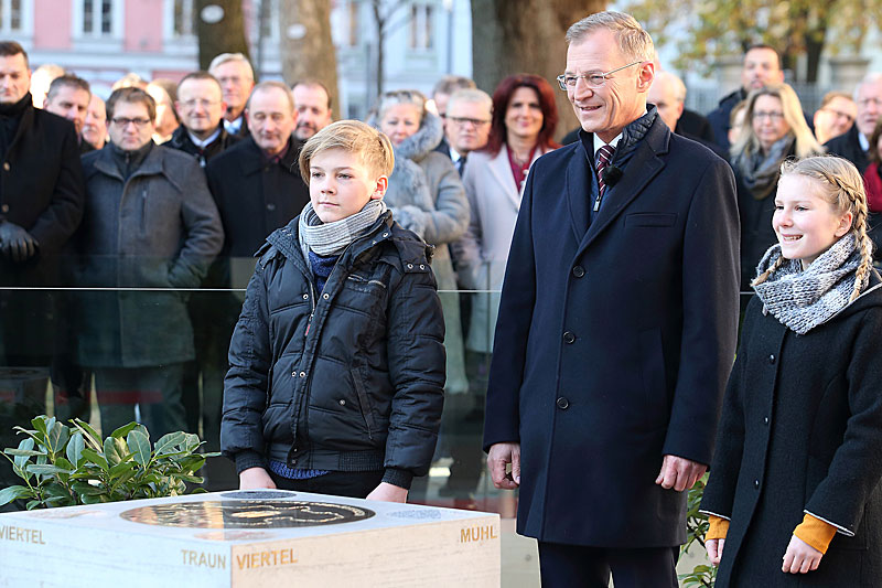 Landeshauptmann Thomas Stelzer mit den Kindern Rosalie Nova und Levin Börner vor dem Gedenkstein